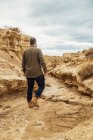 Rückenansicht eines gesichtslosen männlichen Reisenden in lässiger Kleidung in einem schmalen Durchgang zwischen großen braunen Steinen in Bardenas Reales, Navarra, Spanien — Stockfoto