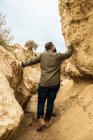 Vue arrière du voyageur masculin sans visage en vêtements décontractés dans un étroit passage entre de grandes pierres brunes à Bardenas Reales, Navarre, Espagne — Photo de stock