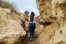 Back view of faceless woman traveler in casual clothing in narrow passage between big brown stones in Bardenas Reales, Navarre, Spain — Stock Photo