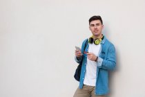 Stylish man in bright headphones surfing mobile phone and holding a credit card while leaning on marble wall — Stock Photo