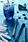 From above fresh blue cocktail with ice cubes and barman equipment with gloves on blue table — Stock Photo