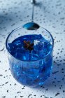 From above bright blue drink with ice cubes in glass with barman spoon on table — Stock Photo