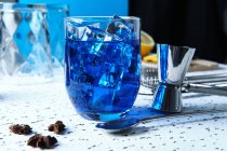 Coquetel azul fresco saboroso com cubos de gelo e ferramentas de barmen na mesa — Fotografia de Stock