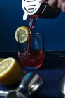 Unrecognizable bartender pouring red cocktail into glass during work on blue counter — Stock Photo