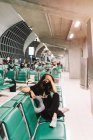Von oben eine besorgte junge Frau mit überkreuzten Beinen und Maske, die den Kopf auf einem Stuhl im Flughafen berührt — Stockfoto