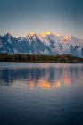 Bezaubernde Landschaft mit hügeligem Ufer und See, die den Sonnenuntergang im Himmel und die schneebedeckten Berge in Chamonix, Mont-Blanc widerspiegelt — Stockfoto