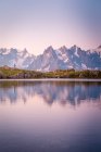 Lonely tourist on hilly shore reflecting in crystal lake in snowy mountains in sunlight — Stock Photo