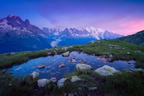 Pietra piccolo lago in erba collina in montagne innevate — Foto stock