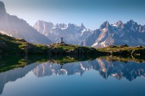 Turista solitario sulla riva collinare che riflette nel lago di cristallo in montagne innevate alla luce del sole — Foto stock
