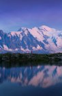 Turista calmo em roupas vermelhas desfrutando de vista montanha refletindo em lago claro em dia ensolarado em Chamonix, Mont-Blanc — Fotografia de Stock