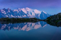 Touriste solitaire sur le rivage vallonné reflétant dans le lac de cristal dans les montagnes enneigées au soleil — Photo de stock