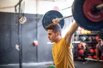 Musculoso chico levantando la barra en el gimnasio moderno - foto de stock