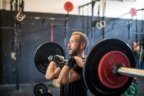 Muscular guy lifting barbell in modern gym — Stock Photo