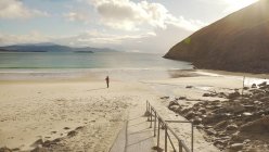 Вид на безликого туриста, созерцающего природу, стоя на песчаном пляже на побережье Ирландии — стоковое фото