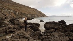 Rückansicht einer unkenntlichen Frau, die an der felsigen Küste Irlands auf das Meer blickt — Stockfoto