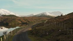 Pintoresco paisaje de carretera de asfalto con valla cerca del río y cadenas montañosas en Irlanda - foto de stock