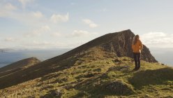Mujer despreocupada disfrutando del maravilloso paisaje natural y el mar mientras está de pie en el acantilado en Irlanda mirando hacia otro lado - foto de stock