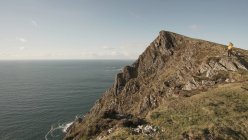 Беззаботная женщина наслаждается прекрасным природным ландшафтом и морем, стоя на скале в Ирландии, глядя в сторону — стоковое фото