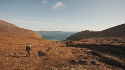 Вид сзади на неузнаваемую женщину, прогуливающуюся по прекрасному природному ландшафту и морю, стоя на скале в Ирландии, глядя в сторону — стоковое фото