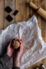 From above crop person holding chocolate dough in hand above white baking paper chocolate metal cookie molds and rolling pin on wooden table — Stock Photo