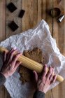 Зверху врожаю людина котиться шоколадне тісто з прокатним штифтом на білому папері для випічки шоколад з металевими формами печива на дерев'яному столі — стокове фото