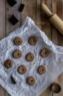 D'en haut biscuits ronds non cuits au chocolat sur papier de cuisson blanc avec moules à biscuits en métal au chocolat et rouleau à pâtisserie sur table en bois — Photo de stock