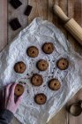 From above anonymous person hand holding chocolate unbaked round cookies on white baking paper with chocolate metal cookie molds and rolling pin on wooden table — Stock Photo