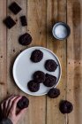 Von oben beschnittene anonyme Hand ergreift aromatische Kekse, die mit Schokoladensirup in einem weißen Teller auf einem Holztisch bedeckt sind — Stockfoto