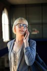 Giovane donna d'affari bionda in occhiali che parla su smartphone e distoglie lo sguardo — Foto stock