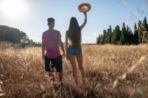 Playful young male standing with female in field with hat in hand — Stock Photo