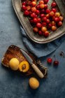 Posa piatta di deliziose ciliegie e pesche gialle servite sul piatto su uno sfondo rustico — Foto stock