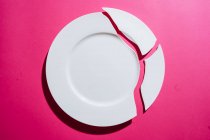 Gebrochener weißer Teller auf rosa Hintergrund — Stockfoto