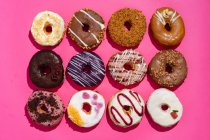 Вид зверху на асортимент смачних солодких глазурованих пончиків, прикрашених глазур'ю та шоколадом — стокове фото