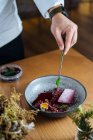 Cropped unrecognizable person preparing on a ceramic bowl with salad made with marinated herring and wild red lingonberries garnished with raw quail egg on wooden table — Stock Photo
