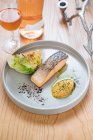 Steamed salmon served with grilled cabbage on white ceramic plate on wooden table with glass and bottle of wine — Stock Photo