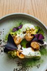 Стейки из белой рыбы с креветками и фиолетовыми листьями базилика на белой тарелке, украшенные зеленым порошком маття на деревянном столе — стоковое фото