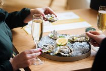 Unrecognizable couple with glasses of champagne trying delicious oysters with lemon and herbs in restaurant — Stock Photo