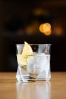 Glass with cold alcoholic cocktail with lemon and ice cubes placed on table against black background — Stock Photo