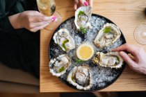 From above top view unrecognizable couple with glasses of champagne trying delicious oysters with lemon and herbs in restaurant — Stock Photo