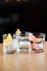 Скляні чашки з холодними алкогольними коктейлями з різними цитрусами, розміщені на столі на чорному тлі — стокове фото