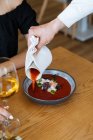 Anonymous waiter pouring tomato sauce into bowl with exquisite rice dish with vegetables and herbs for client during dinner in restaurant — Stock Photo