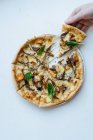 Overhead anonymous person taking slice of palatable seafood pizza with mushrooms and basil against white background — Stock Photo