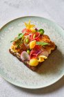 De cima sanduíche saboroso decorado com legumes fatiados e flores e colocado na placa na mesa branca no café — Fotografia de Stock