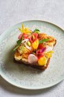 De cima sanduíche saboroso decorado com legumes fatiados e flores e colocado na placa na mesa branca no café — Fotografia de Stock