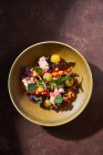 Вид сверху на миску с вкусным крабовым салатом со свежими овощами и зеленью, поставленным на коричневый стол — стоковое фото