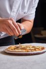 Cuoco irriconoscibile che affetta il tartufo fresco su una gustosa pizza mentre lavora nel ristorante — Foto stock