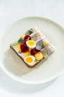 Вкусный рыбный сэндвич со свежими овощами и вареными яйцами перепела на тарелке в кафе — стоковое фото