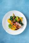 Top view from above tasty roasted meat served with pieces of mango and pumpkin on plate in restaurant — Stock Photo