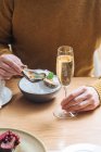 Persona recortada irreconocible con copas de champán probando deliciosas ostras con limón y hierbas en el restaurante - foto de stock