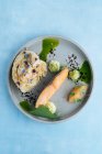 Сверху выпечки филе лосося и икры щуки с кусочком молодой капусты на стильной серой тарелке, украшенной белым соусом на синем фоне — стоковое фото